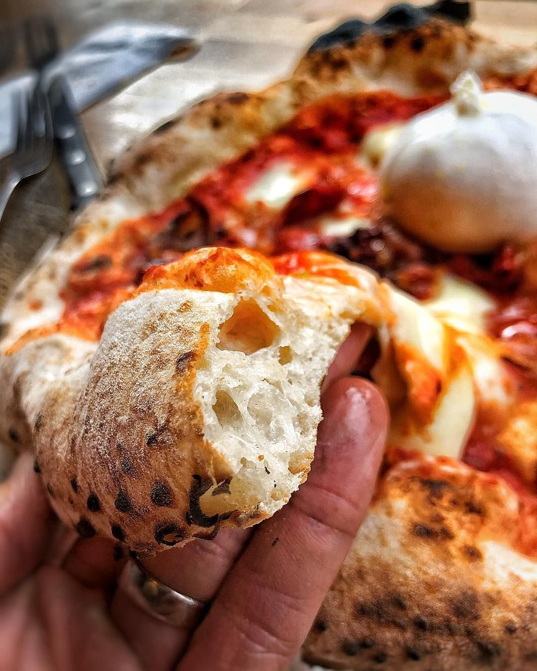 A hand tearing open an airy, leopard-spotted pizza crust